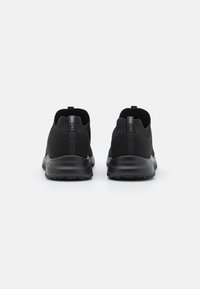 Zwarte sportieve schoenen met een gebreide bovenkant, voorzien van een pull-tab aan de hiel en een gestreepte zool voor grip. Eenvoudig, gestroomlijnd ontwerp.