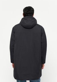Manteau rembourré noir long avec capuche, présentant une texture lisse et un design minimaliste. L'arrière est dépouillé avec un ourlet droit.