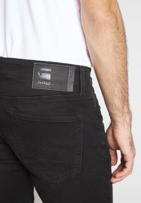 Černé džínsy z denimu s koženou nášivkou sembossovaným logem, detaily zadní kapsy a těsným střihem. Látka vypadá hladce.