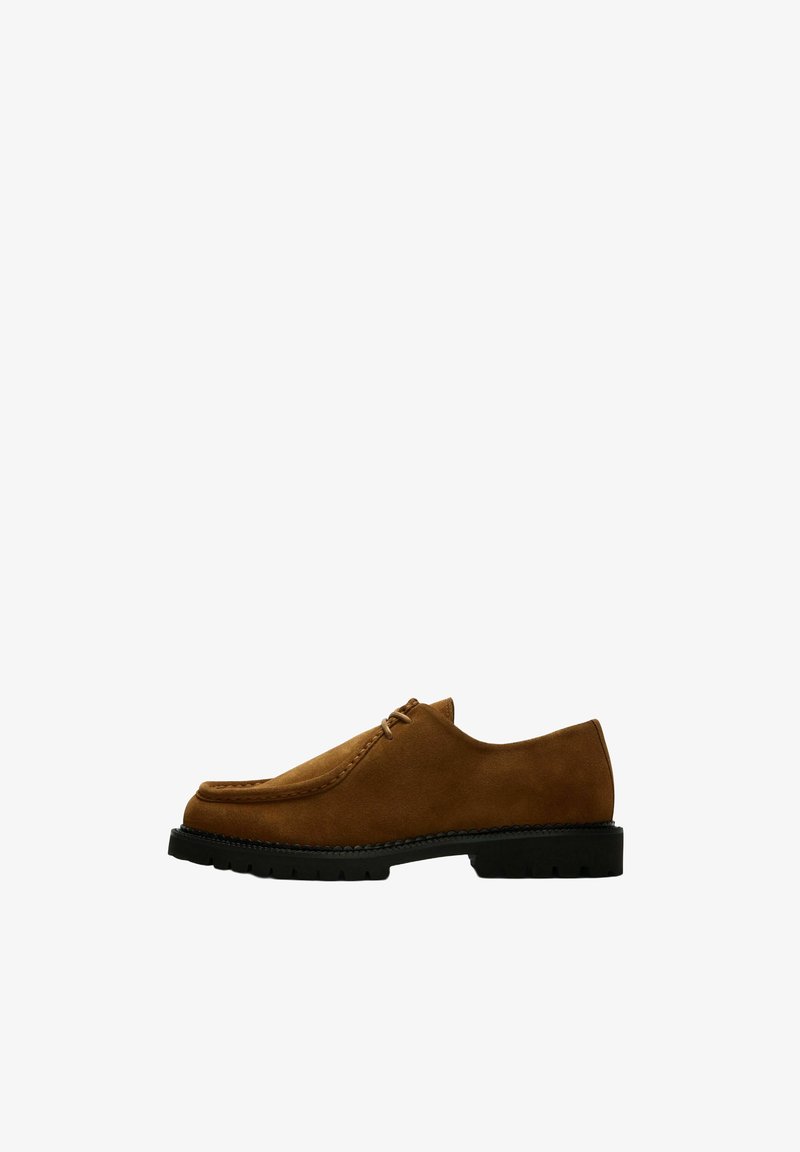 Chaussure à lacets en daim marron avec semelle noire épaisse, couture moc toe et petit talon, vue de côté sur fond blanc.