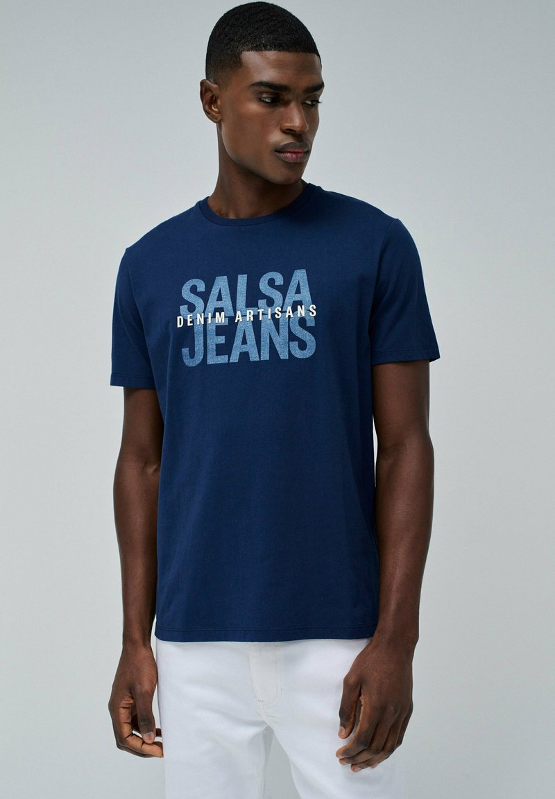 Camiseta de algodón azul marino de manga corta y cuello redondo, con "SALSA JEANS" y "DENIM ARTISANS" impresos en texto grueso en blanco y gris.