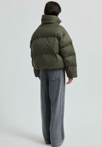 Olivgrön puffjacka med hög krage, med ett quiltat mönster. Matchas med lösa jeansbyxor i medelblå tvätt.