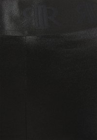 Leggings neri con una superficie liscia e lucida. Caratterizzati da una vita alta con un logo nero. Il tessuto sembra elastico e aderente.