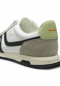 Baskets pour hommes avec cuir suédé blanc et beige, panneau de talon vert, bande noire et semelle claire texturée avec crampons noirs.