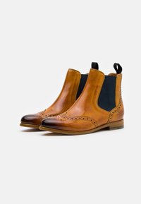 Botas Chelsea de cuero marrón con puntera pulida, paneles elásticos laterales en contraste, detalles decorativos de brogue y un tacón plano.