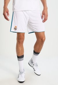 Valkoiset urheilushortsit, joissa on teal-väriset yksityiskohdat ja Real Madridin logo. Yhdistetty harmaaraidallisiin sukkiin ja valkoisiin lenkkarikenkiin. Kevyt ja hengittävä kangas.