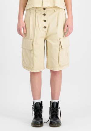 Person wearing beige knee-length cargo shorts with front buttons and black lace-up boots with white socks.