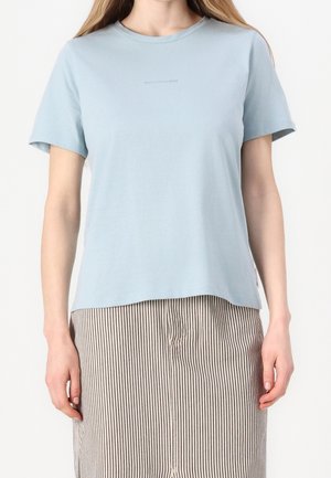 Woman wearing a light blue short-sleeve t-shirt paired with a beige and black vertical striped skirt against a white background.