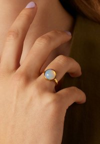 Goldring mit einem glatten blauen Edelstein. Der Band ist schlank, und der Stein ist rund mit einem subtilen schimmernden Effekt. Hand natürlich positioniert.