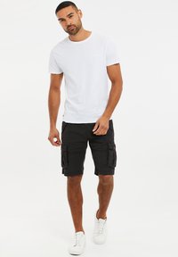 Camiseta de algodón blanca combinada con pantalones cortos cargo negros con bolsillos laterales y zapatillas blancas. Diseño simple y casual.