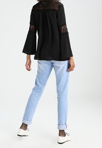 Czarna bluzka z koronkowymi akcentami na rękawach, zestawiona z jasnoniebieskimi dżinsami z podwiniętymi nogawkami i białymi butami. Bluzka ma luźny krój i długie rękawy.