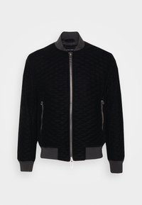 Svart kviltad bomberjacka med dragkedja fram, ribbade ärmslut och krage i kontrasterande grått tyg. Har sidofickor med dragkedja.