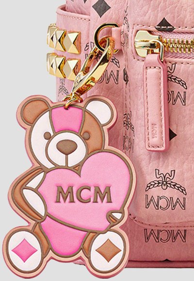 Borsa in pelle rosa con hardware dorato, dotata di un portachiavi a forma di orsetto in cioccolato che tiene un cuore rosa con "MCM" scritto in lettere marroni.