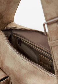 Beige suede handbag interior with a smooth texture, featuring a zippered pocket and beige lining. Includes a branded leather tag.
