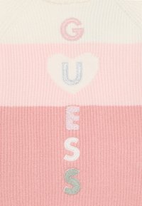 Maglione a righe rosa e crema con "GUESS" ricamato in lettere multicolori; la texture è a costine con un morbido dettaglio a forma di cuore.