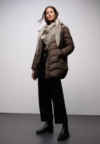 Brun vatteret jakke med hætte, gråt tekstureret tørklæde, mørke bukser og sorte ankelstøvler. Glat stof og oversized pasform.