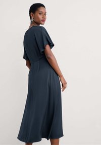 Tumma sininen mekko, jossa on lyhyet levyiset hihat, istuva yläosa ja lentävä A-linjainen hame. Hieno kangas, joka hehkuu hieman. Takana vetoketjusuljenta.