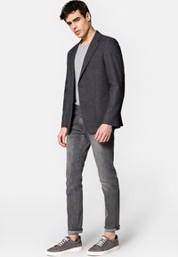 Szary w kratę marynarka z klapami, zestawiona z jasnoszarym t-shirtem i węższymi szarymi dżinsami. Szare zamszowe trampki dopełniają strój.