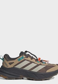 Καφέ και μπεζ πεζοπορικό παπούτσι Adidas Terrex με μαύρη σόλα, λεπτομέρειες κορδονιών σε τιρκουάζ και πορτοκαλί χρώμα, και σόλα με πρόσφυση Continental.