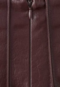 Superficie de cuero sintético burdeos con un acabado ligeramente texturizado, que presenta una cremallera central y detalles de costuras verticales.