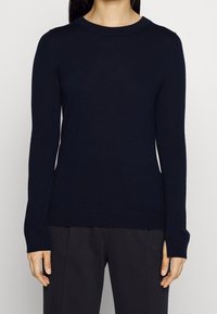 Pull à manches longues bleu marine avec un col rond, fabriqué en tissu doux. Présente une silhouette ajustée ainsi que des poignets et un ourlet côtelés.