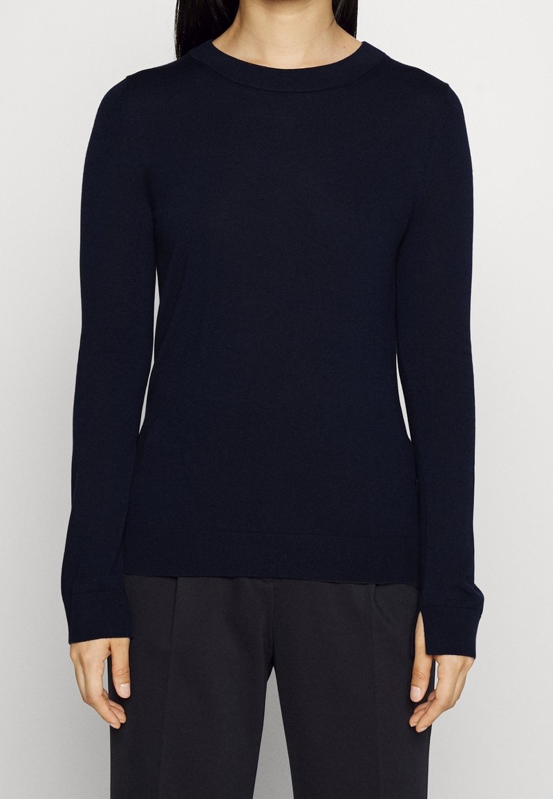 Pull à manches longues bleu marine avec un col rond, fabriqué en tissu doux. Présente une silhouette ajustée ainsi que des poignets et un ourlet côtelés.