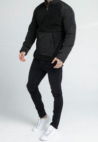 Jacket nera a pullover realizzata in pile e nylon, con zip a quarto, tasca a marsupio e maniche con contrasto testurizzato. Abbinata a jeans neri e sneakers bianche.