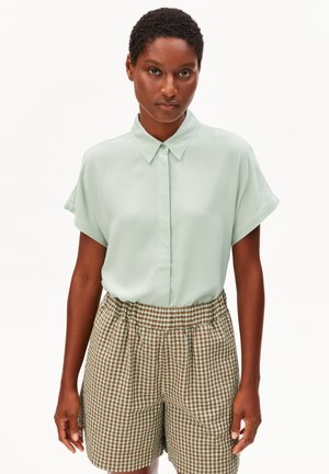 Hellgrünes Kurzarmhemd mit Knöpfen am Kragen, kombiniert mit braun-grünen Gingham-Karo-Shorts mit elastischem Bund.