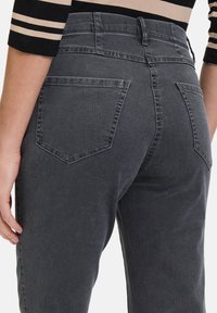 Ciemnoszare dżinsy o dopasowanym kroju, z dwoma tylnymi kieszeniami i wysokim stanem. Tkanina ma subtelną fakturę.