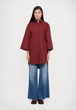 Burgundia suuruses särk terava kraega, laiad varrukad ja rinnatasku, koos laia säärega pleekinud denimplaadiga.