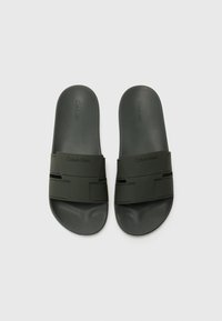 Melni gumijas slidināšanas sandales ar teksturētu zolīti un široku siksnu ar ģeometriskiem izgriezumiem. Uz siksnas ir izdrukāts logotips.