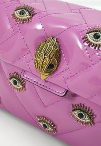 Lila lackhandväska med kviltat mönster, prydd med metalliska ögonförsköningar och en dekorativ guldspänne i form av en fjäder.