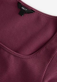 Burgundský ribbed top s širokým výstřihem a sešitými švy. Na výstřihu se nachází černá visačka s nápisem "NEXT".
