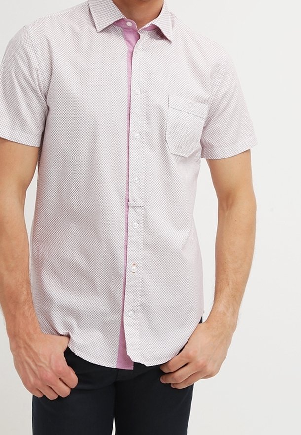 Man met een lichtroze, kortgewijd patroon overhemdd met een borstzak, gecombineerd met donkere broek.