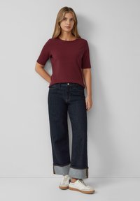 Bordo ribota īsām piedurknēm blūze apvienota ar tumši ziliem platām džinsu biksēm ar locītavu un gaiši pelēku denimu akcentiem. Balti sporta apavi pabeidz izskatu.