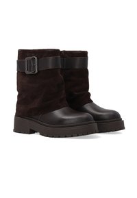 Brązowe zamszowe botki za kostkę z gładkim skórzanym noskiem, grubą podeszwą z bieżnikiem oraz szerokim regulowanym paskiem z metalową klamrą w kolorze srebrnym.