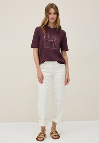 Sudadera corta de manga larga color burdeos con un gráfico que dice "CURIOUS", combinada con jeans blancos de puño enrollado y sandalias marrones. Tejido ligero y casual.