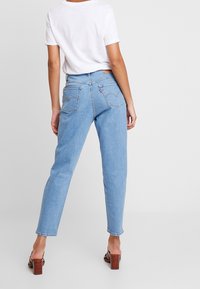 Ljust blå raka jeans med medelhög midja, bakfickor med en sydd design och en vit T-shirt som bärs instoppad.