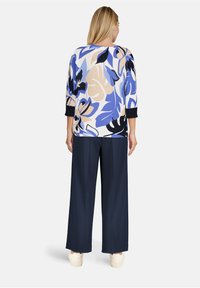 Pull en tricot bleu, crème et noir avec un motif floral, associé à un pantalon large marine et des baskets légères ; manches trois-quarts.