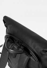 Zaino nero realizzato in materiale testurizzato, con chiusura a rotolo, due zip e una maniglia superiore per il trasporto.