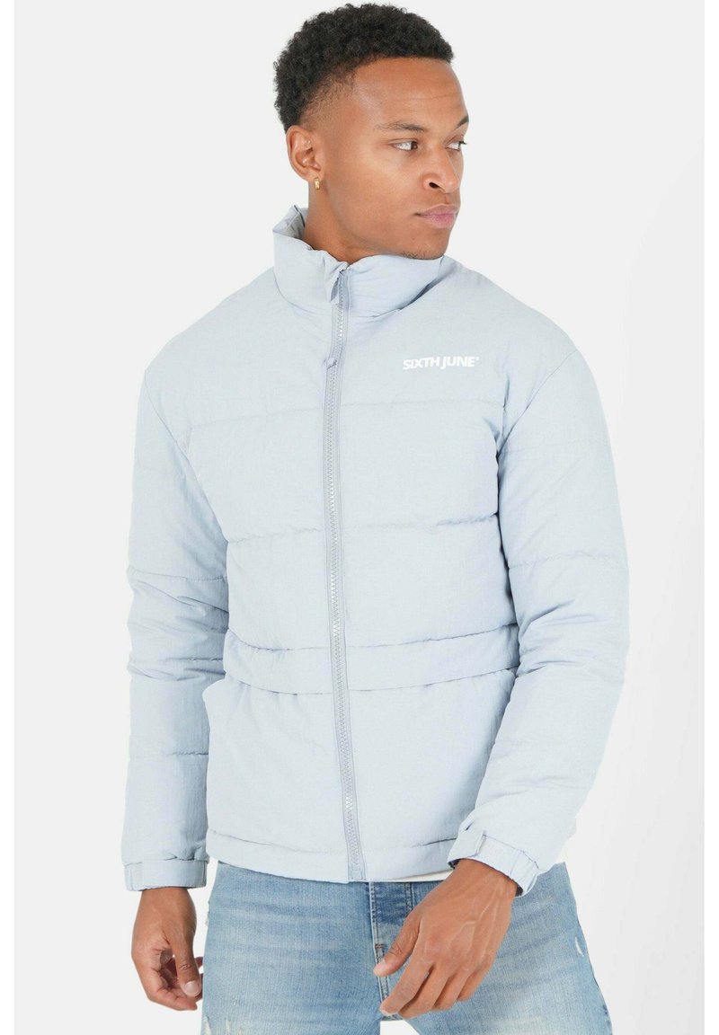 Giacca puffer azzurro chiaro con design trapuntato, colletto alto e cerniera frontale. Presenta un logo bianco sul petto e polsini a coste.