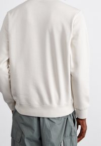 White sweatshirt with a smooth texture, ribbed cuffs, and hem. Designed with a classic crew neck and a relaxed fit.