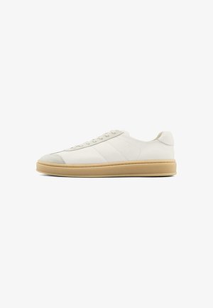 White suede sneakers with a smooth texture, round toe, lace-up front, and a tan rubber sole. Features subtle side stripes and heel accents.