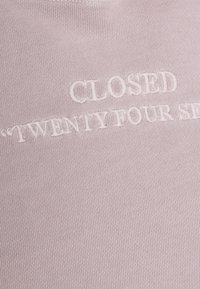 Světle růžový pletený svetr s vyšitým textem "CLOSED TWENTY FOUR SEVEN" v mírně tmavší růžové přízi.