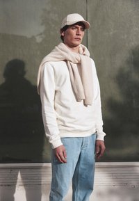 Felpa crema, sciarpa beige chiaro, jeans azzurri chiari e cappellino beige. Texture liscia, vestibilità comoda, design minimalista. Palette di colori tenue.