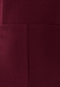 Bordeauxfarbener Stoff mit weicher Textur und sichtbaren Nähten. Zeichnet sich durch ein sauberes, maßgeschneidertes Design mit glattem, gleichm�äßigem Erscheinungsbild aus.