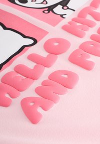 Opgeblazen roze letters op lichtroze stof spellen "HELLO MADAME" met een deel van een zwart-wit cartoonfiguur boven de tekst.