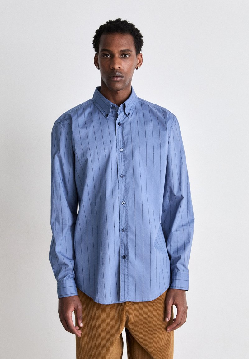 Camicia azzurro chiaro con bottoni, a righe verticali, maniche lunghe e colletto a punta. Realizzata in tessuto morbido con una vestibilità comoda.