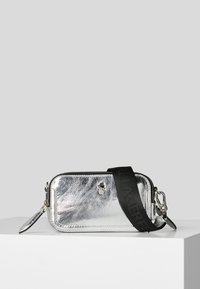 Piccola borsa a tracolla rettangolare in metallo argentato con tracolla nera regolabile e ornamento in metallo a forma di teschio sulla parte anteriore.