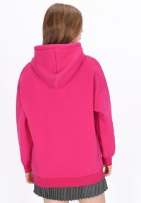 Sudadera con capucha de color rosa brillante, con una gran capucha, ajuste relajado y puños acanalados. La tela parece suave con una textura lisa.